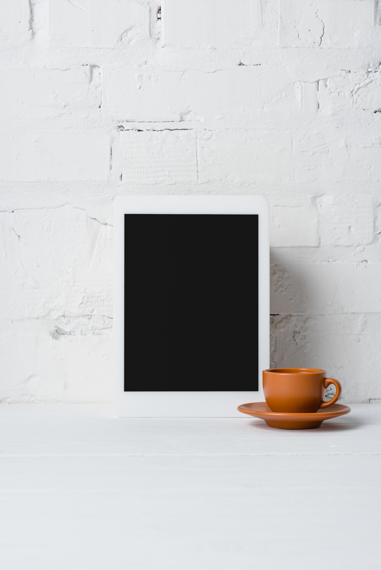 close-up view of digital tablet with blank screen and cup of coffee near white brick wall