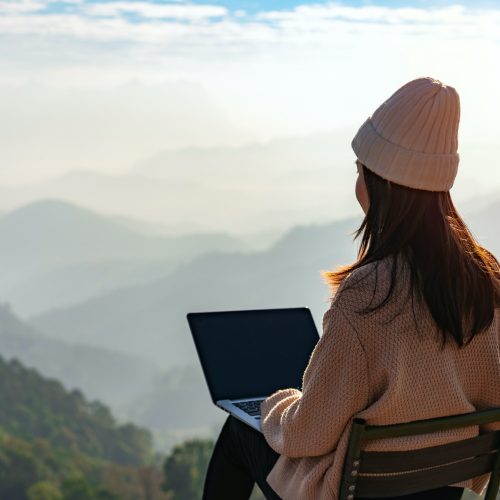 Young woman freelancer working online using laptop and enjoying the beautiful nature landscape